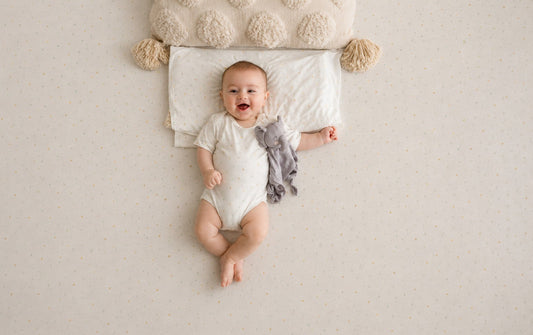 A baby gift set arranged next to a baby, featuring bamboo baby clothing, a light blanket or swaddle, burp cloths, and a simple baby book.